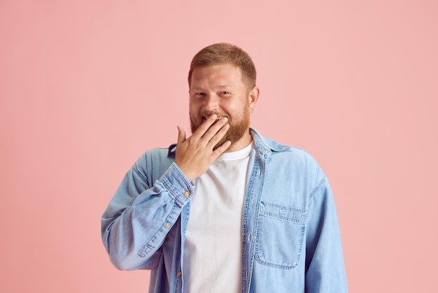 분홍색 스튜디오 배경에서 손으로 입을 가리고 웃고 있는 평상복 차림의 명랑한 남자 인간의 감정 라이프스타일 표정 광고 개념 광고 공간 복사