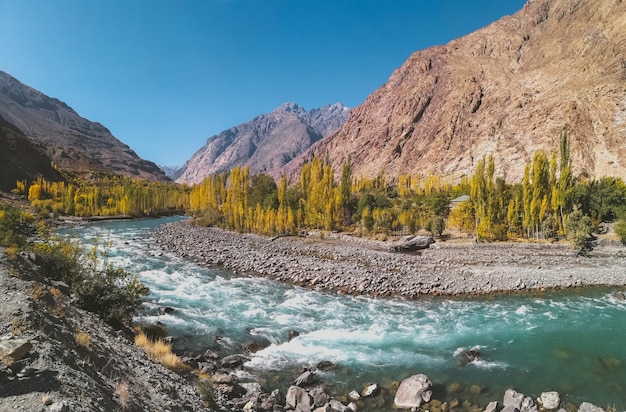 Photo gilgit river flowing through gupis, with a view of mountain range and trees in autumn.