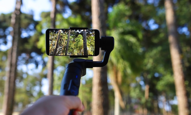 Gimbal. Young man using stabilizer for cell phone and filming the forest. Selective focus.