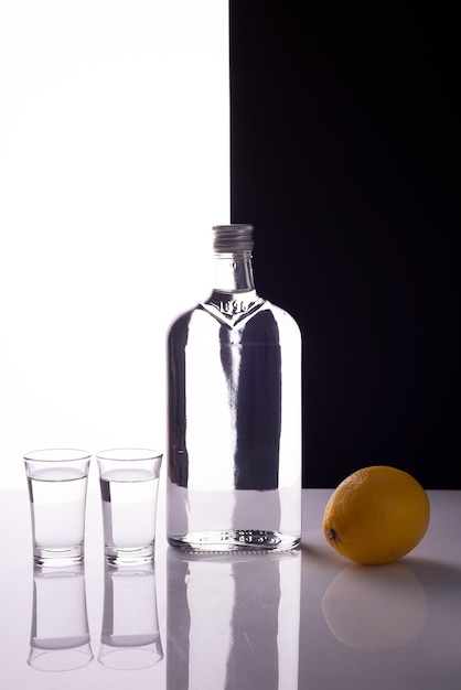 Gin bottle with shot glasses on black and white background alcoholic drink with lemon