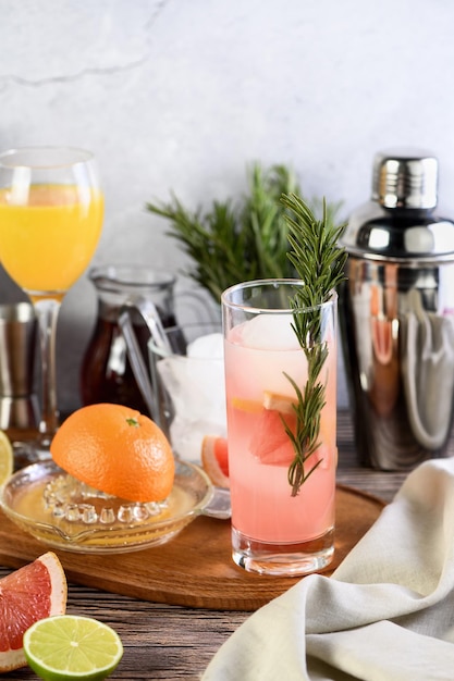 Gin cocktail with rosemary and pomegranate on a table among citrus fruits and drinks.