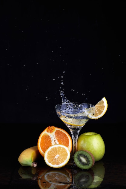 Gin tonic cocktail with fruits, splashes and lemon on isolated black