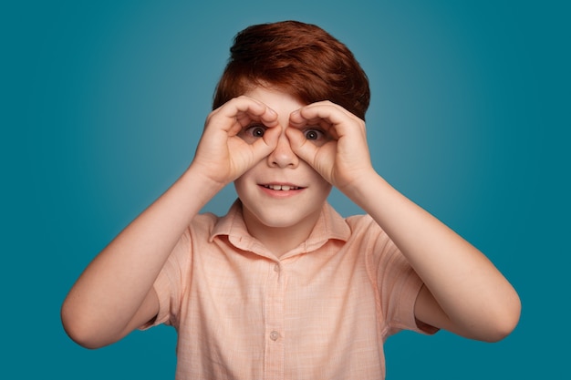 Ginger boy gesturing binocle sign on studio in trendy style fashion model