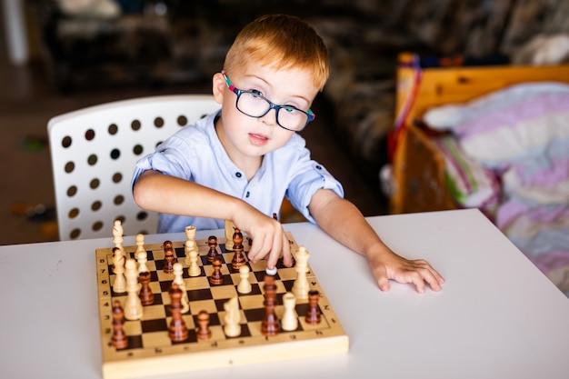 Ginger boy with down syndrome with big glasses playing chess at home