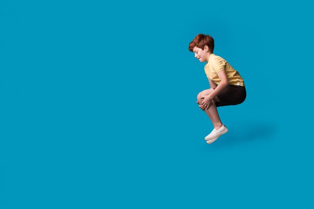 Ginger caucasian boy gesturing a jump in pool while smile and promoting something on a blue studio