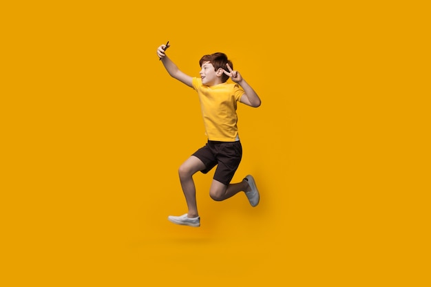 Photo ginger caucasian boy jumping on a yellow studio wall and making a selfie