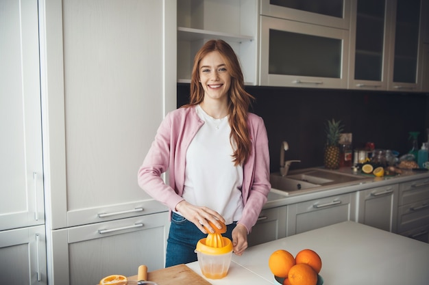 Ginger caucasian lady with freckles smiling at camera while squeezing fruits and making juice