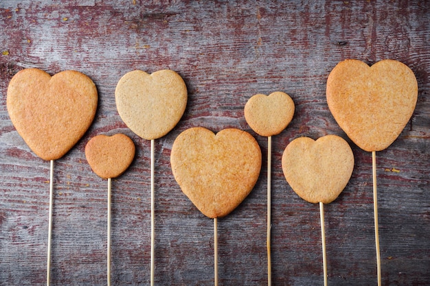 Biscotti allo zenzero su un bastone a forma di cuori allineati su un tavolo di legno.