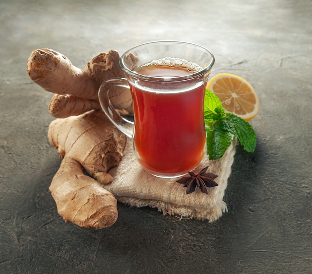 Photo ginger drink in a transparent glass mug. next to it is ginger root, cardomom, mint and lemon.