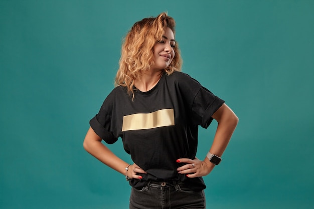 Ginger girl with a curly hair wearing black tshirt with a golden stripe is posing