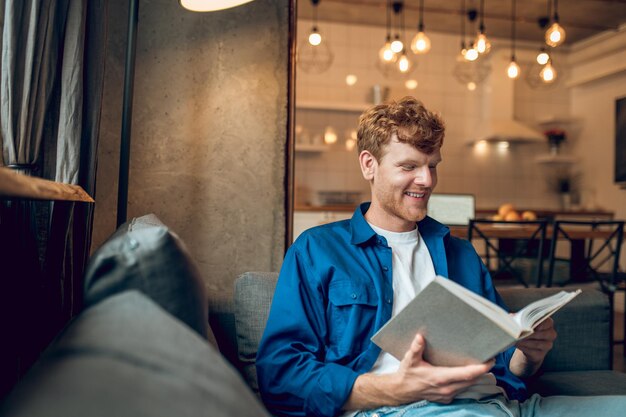 Ginger jonge man zit thuis bij het raam met een boek