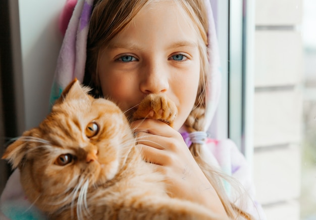 Ginger kitten en een klein meisje zitten op de vensterbank en kijken uit het raam.