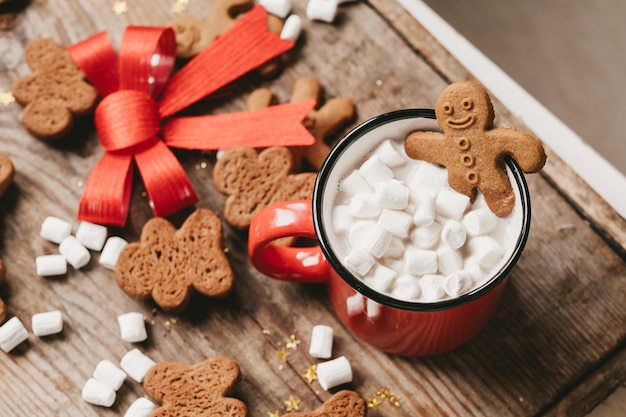 Ginger man in een kopje cacao met een grote rode strik op een houten ondergrond, bovenaanzicht. diverse kerstsnoepjes met een kopje cacao op tafel. kerst flatlay