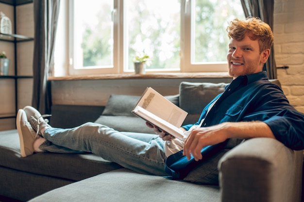 A ginger man sitting at the window and reading a book