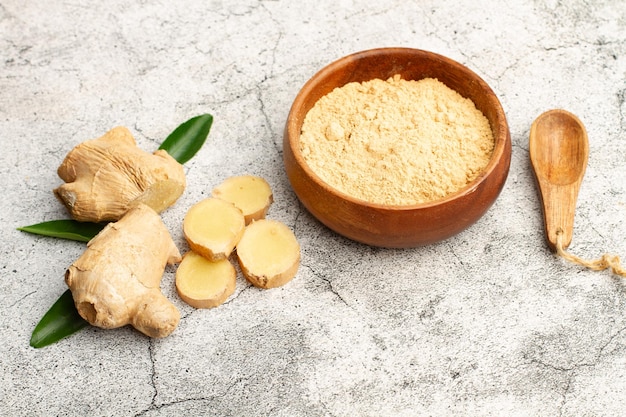 Ginger powder in a wooden bowl and a ginger root on a stone background with copy space