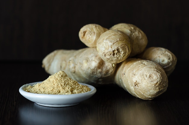 Ginger root and powder on dark wooden table. eco food