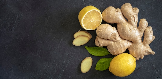 Radice di zenzero con limone giallo e foglie verdi su sfondo scuro, copia spazio, copyspace, vista dall'alto