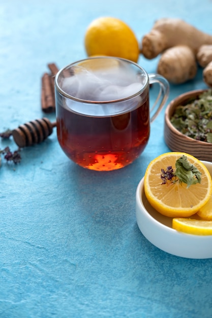 Ginger tea with lemon in glass cup at blue surface