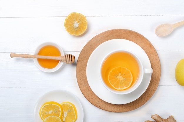 Имбирь с лимоном и травяным чаем на деревянном столе на белом фоне