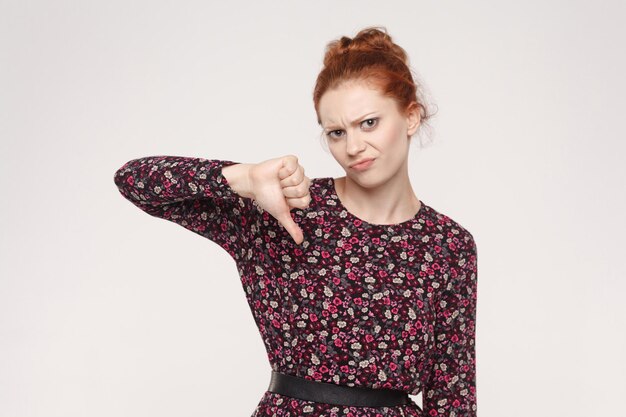 Ginger woman showing thumb down isolated on a gray background