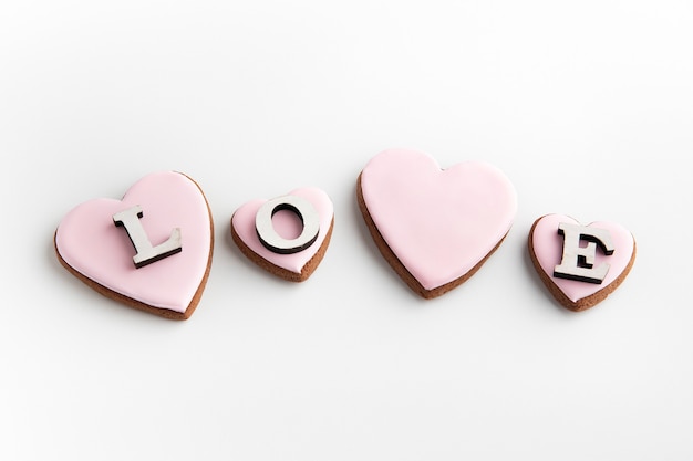 Photo gingerbread cookies in heart-shaped with pink sugar icing on white background and inscription love.