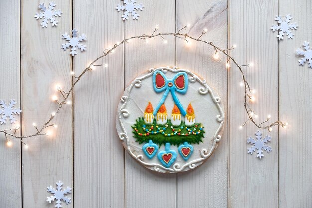 Gingerbread decorated with advent wreath with candles and hearts. creative traditional gifts for children. christmas flat lay with snowflakes, garland of lights. rustic off white wooden table