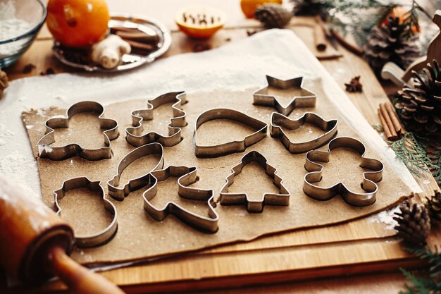 Gingerbread dough with metal cutters in different shapes for\
christmas cookies and wooden rolling pin anise ginger cinnamon pine\
cones fir branches flour on rustic table