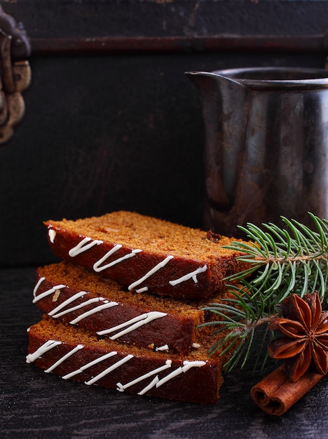 Gingerbread (honey-cake) with raisins decorated with icing, spruce branches, cinnamon sticks, star anise on a black background