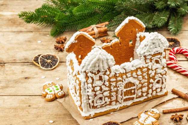 Gingerbread House decorated by sweet icing. Handmade process, festive New Year decor. Traditional spices, wooden background