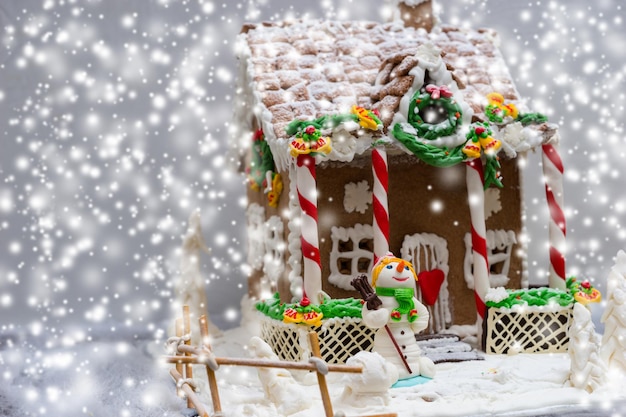 Gingerbread house, gingerbread Christmas tree and a sugar mastic snowman during snowfall. Mockup for seasonal offers and holiday post card