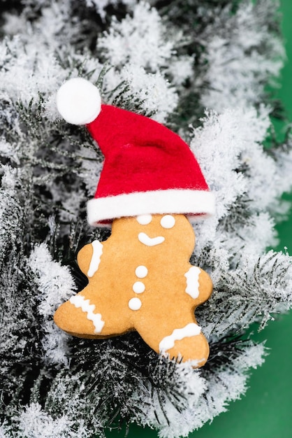 Gingerbread man in santa hat on fir branch with decorative snow