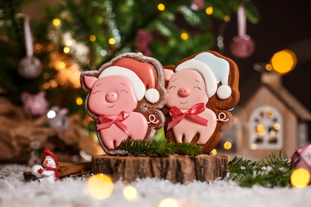 Пряники две счастливые розовые свиньи в новогодней шапке в уютном теплом декоре с гирляндой подсветкой