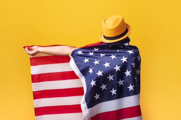 Gir with American flag over yellow background, girl in fashionable hat with USA flag