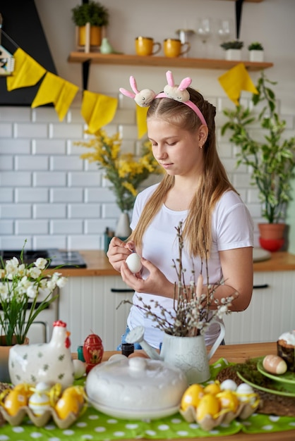 Фото Двенадцатилетняя девочка рисует яйца на пасху на кухне.