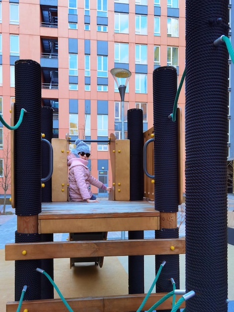 Photo the girl 9 years old on the playground the child is dressed in warm demiseason clothes a pink jacket and a grey hat