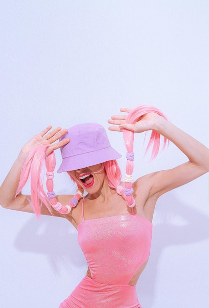 白いスタジオでポーズをとる90年代の女の子のパーティーヒップホップスタイル。トレンディなピンクのジャンプスーツ、バケツの帽子、ピンクの髪。ファッションユニコーンレディバイブ