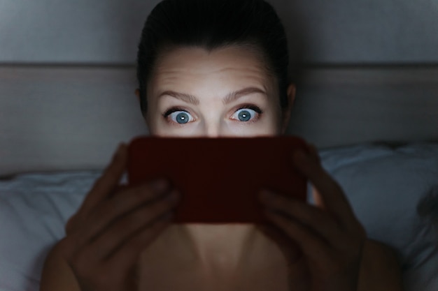 Girl addictively staring at her smartphone late at night in bed.