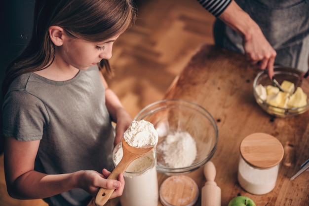 Girl adding flour into mixing bowl