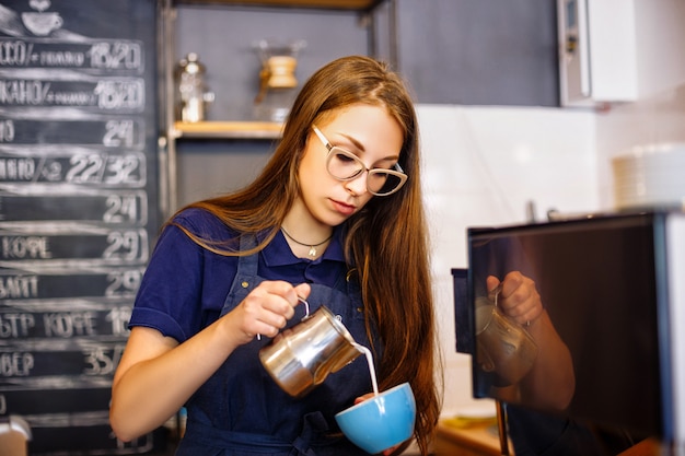 The girl adds milk to the cup with coffee in cafe