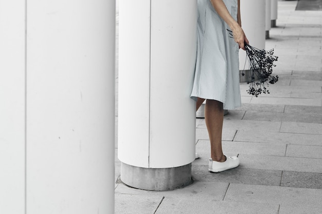 A girl against the background of round white pillars holds a branch in her hands. Geometry in buildings, city walks. Copy space.