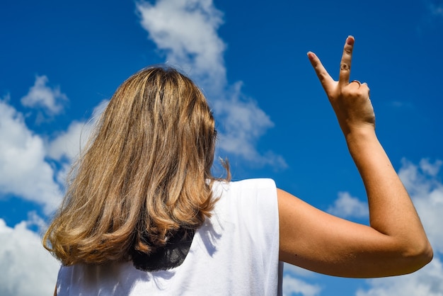 the girl against the sky with her back to the camera depicts a victory hand