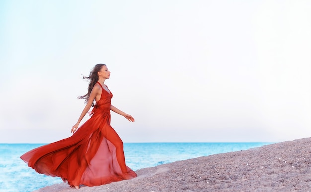 Девушка в воздушном платье бежит по пляжу