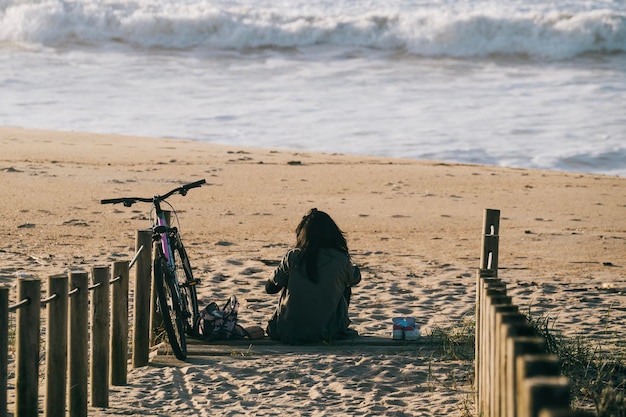 Girl alone with a bicycle sitting on the beach relaxed and calm in front of sea waves