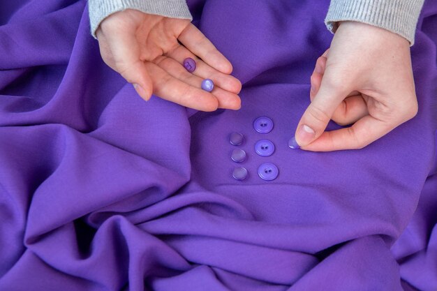 The girl applies buttons of matching color to the purple fabric Hobby sewing