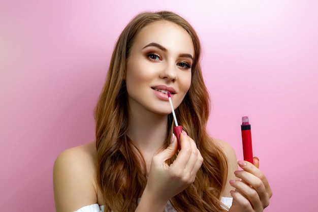 Photo girl applying lipstick on a pink background