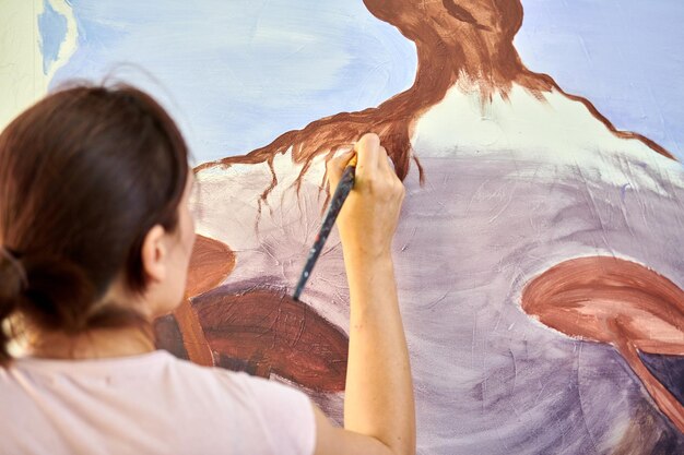 Foto la mano dell'artista ragazza tiene il pennello e disegna un paesaggio naturale astratto su tela