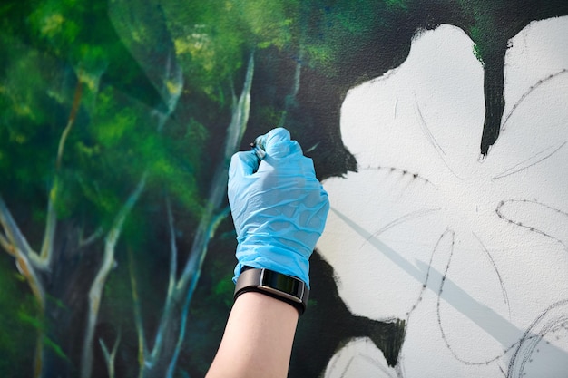 女の子アーティストの手は絵筆を持ち、キャンバスに緑の自然の風景を描きます