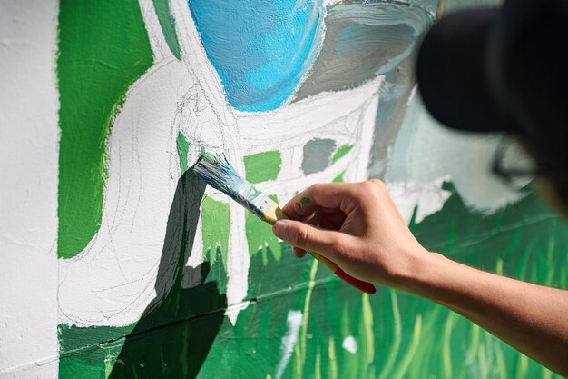 Girl artist hand holds paint brush and draws green nature landscape on canvas