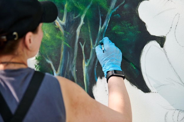 Girl artist hand holds paint brush and draws green nature landscape on canvas