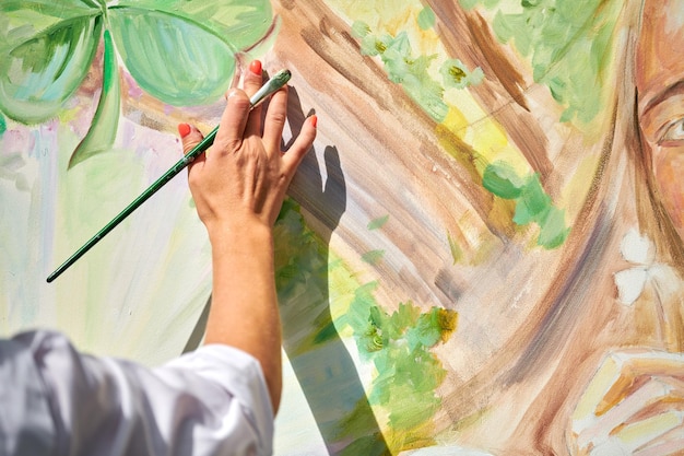 Girl artist hand holds paintbrush and draws green nature landscape on canvas